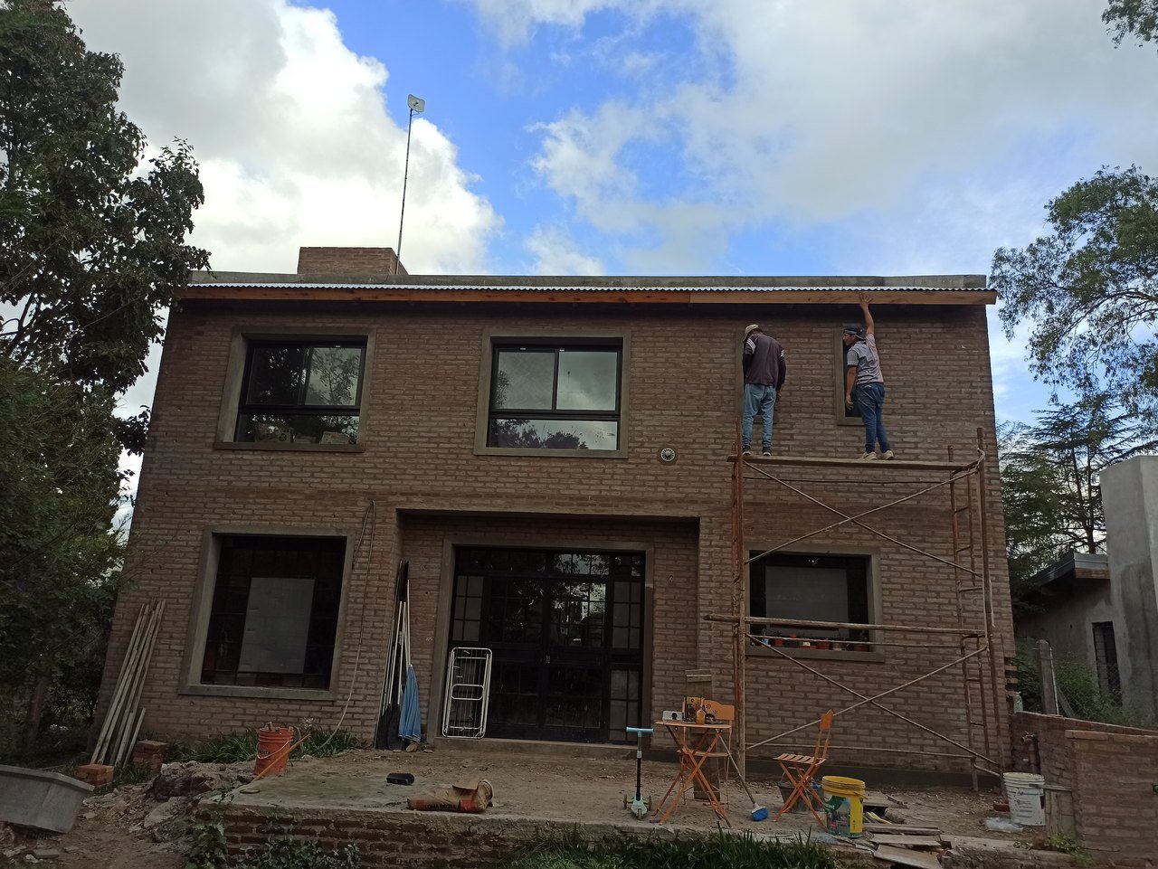 Casa de ladrillo y pérgola: fachada con andamios (en obra)